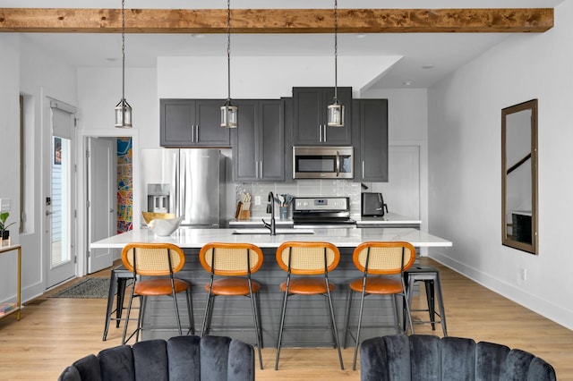 kitchen featuring stainless steel appliances, a center island with sink, and decorative light fixtures