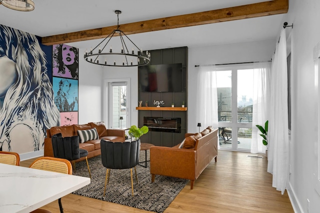 living room featuring a fireplace, beamed ceiling, a chandelier, and light hardwood / wood-style flooring