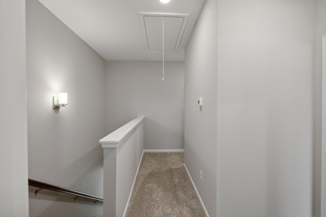 hall featuring attic access, an upstairs landing, baseboards, and carpet floors