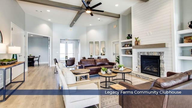 living room featuring light hardwood / wood-style flooring, beam ceiling, a high ceiling, and a stone fireplace