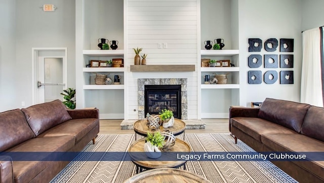 living room featuring wood-type flooring, built in features, and a stone fireplace