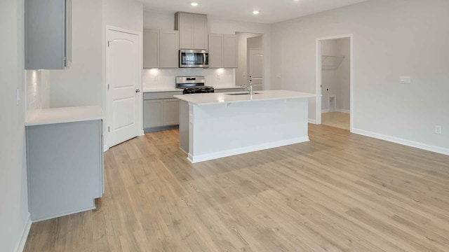 kitchen featuring sink, light wood-type flooring, gray cabinets, an island with sink, and stainless steel appliances