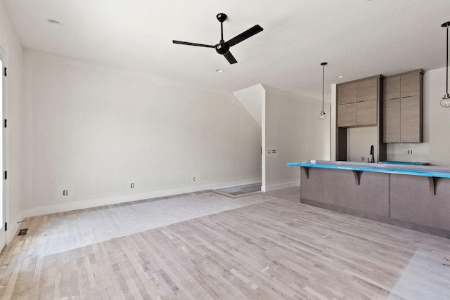 kitchen featuring decorative light fixtures, light hardwood / wood-style floors, gray cabinets, ceiling fan, and a breakfast bar area