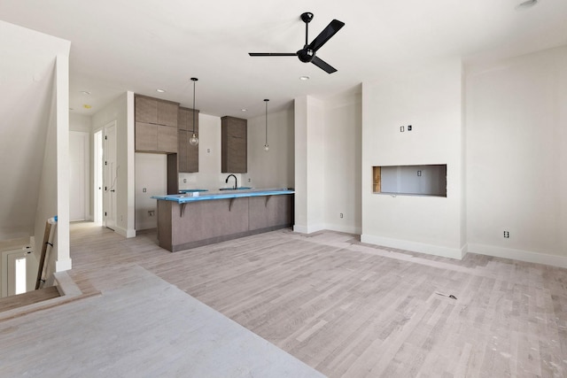 kitchen with pendant lighting, ceiling fan, sink, a kitchen bar, and light hardwood / wood-style floors