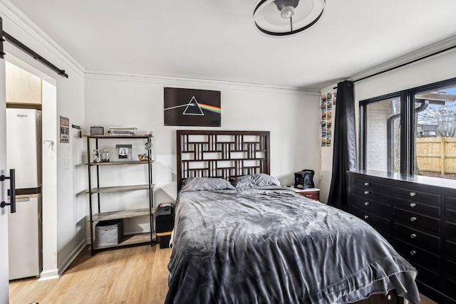 bedroom featuring crown molding, light hardwood / wood-style floors, fridge, and a barn door