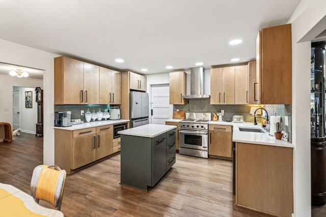 kitchen with a center island, wall chimney exhaust hood, stainless steel appliances, sink, and light hardwood / wood-style flooring