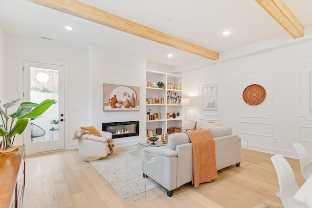 living room featuring built in features, beam ceiling, and light wood-type flooring