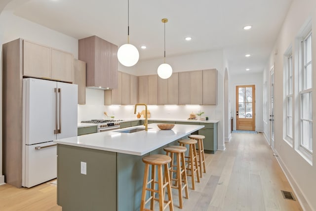 kitchen featuring hanging light fixtures, high quality range, white fridge, and an island with sink