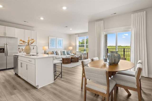 kitchen with white cabinets, light hardwood / wood-style flooring, stainless steel appliances, sink, and a center island with sink