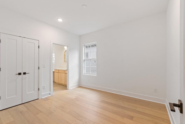 unfurnished bedroom featuring a closet, light hardwood / wood-style floors, and ensuite bath