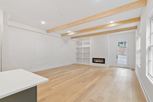 unfurnished living room with built in shelves, beamed ceiling, and hardwood / wood-style flooring