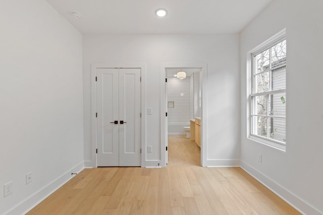 unfurnished bedroom with a closet, ensuite bathroom, and light hardwood / wood-style flooring