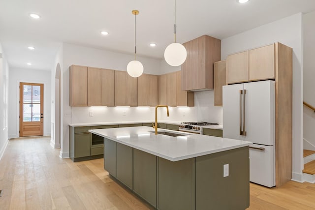 kitchen with white refrigerator, green cabinets, pendant lighting, and a center island with sink