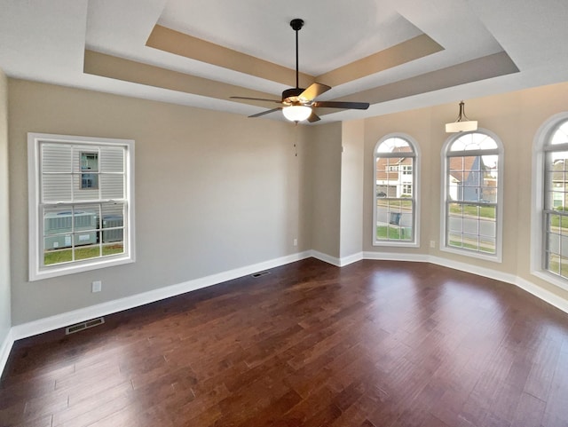 spare room with dark hardwood / wood-style floors, ceiling fan, and a raised ceiling