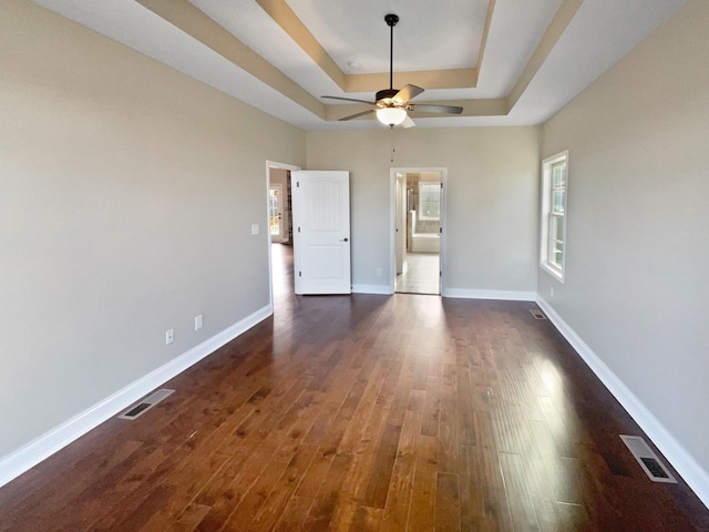 unfurnished bedroom featuring dark hardwood / wood-style floors, ceiling fan, and a raised ceiling