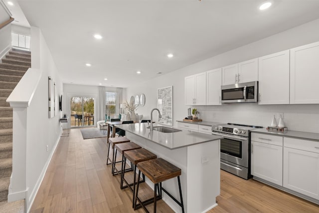 kitchen featuring a kitchen bar, white cabinetry, stainless steel appliances, sink, and a center island with sink