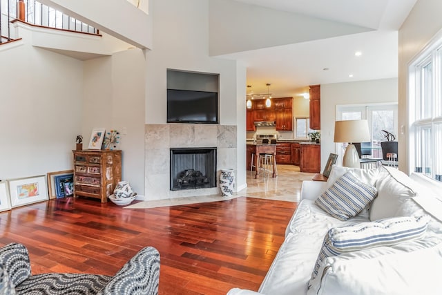 living room featuring hardwood / wood-style flooring, high vaulted ceiling, and a tiled fireplace