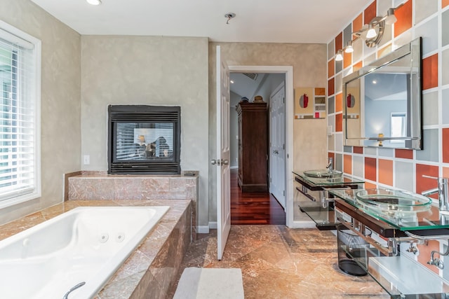 bathroom featuring vanity, a multi sided fireplace, and tiled tub