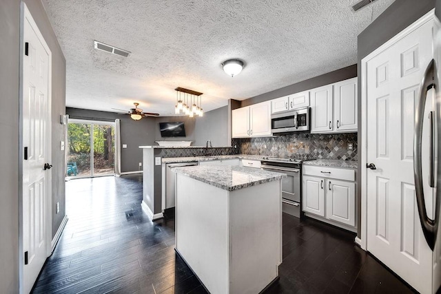 kitchen featuring white cabinets, appliances with stainless steel finishes, decorative light fixtures, decorative backsplash, and kitchen peninsula