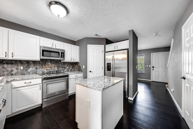 kitchen featuring light stone countertops, white cabinets, appliances with stainless steel finishes, a kitchen island, and decorative backsplash