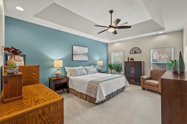 bedroom with ceiling fan, light colored carpet, and a tray ceiling