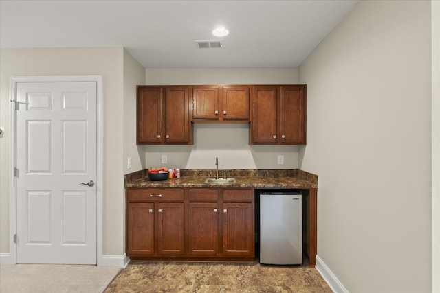 kitchen featuring sink, dark stone countertops, and stainless steel refrigerator