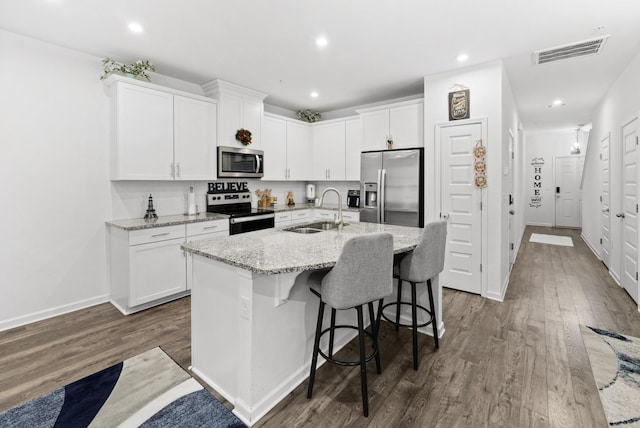 kitchen featuring sink, stainless steel appliances, light stone countertops, white cabinets, and a center island with sink