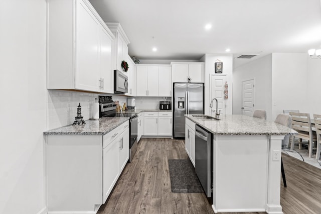 kitchen with sink, an island with sink, stainless steel appliances, light stone countertops, and white cabinets