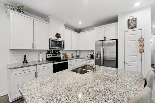 kitchen featuring sink, stainless steel appliances, light stone counters, an island with sink, and white cabinets