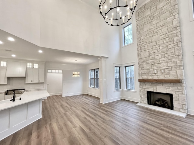 unfurnished living room with a towering ceiling, a fireplace, hardwood / wood-style floors, a healthy amount of sunlight, and a notable chandelier