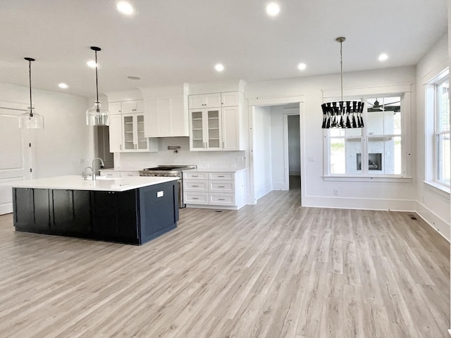 kitchen with white cabinetry, light wood-type flooring, pendant lighting, high end stainless steel range oven, and a center island with sink