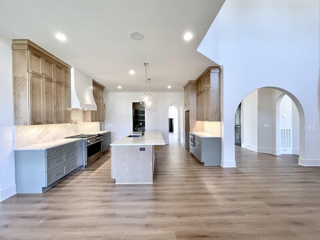 kitchen featuring pendant lighting, sink, hardwood / wood-style flooring, a center island with sink, and high end stove