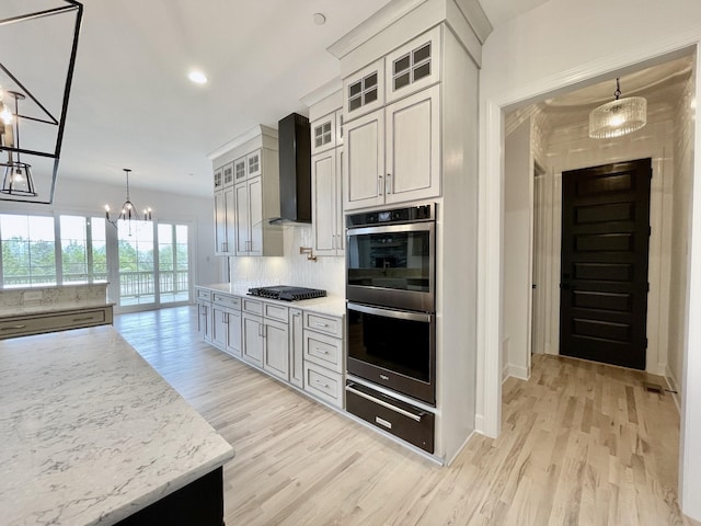 kitchen with wall chimney exhaust hood, multiple ovens, white cabinetry, and hanging light fixtures