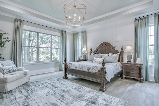 bedroom with hardwood / wood-style floors, an inviting chandelier, and a tray ceiling