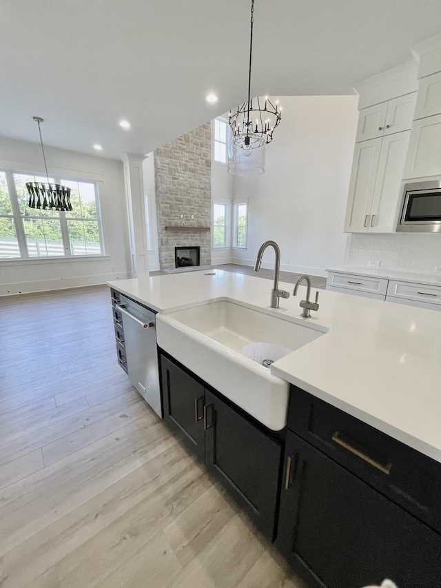 kitchen with pendant lighting, appliances with stainless steel finishes, sink, white cabinetry, and light hardwood / wood-style floors