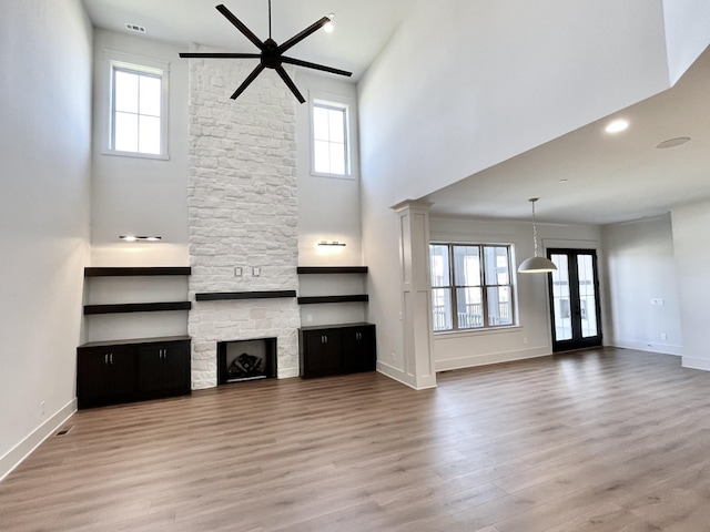 unfurnished living room featuring a wealth of natural light, a high ceiling, hardwood / wood-style floors, and a stone fireplace