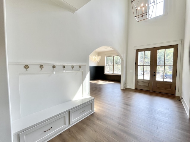 mudroom with an inviting chandelier, light hardwood / wood-style flooring, a towering ceiling, and french doors