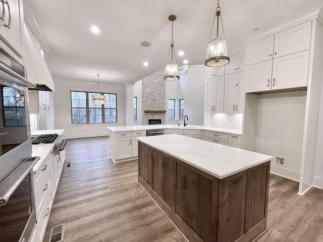 kitchen featuring white cabinets, decorative light fixtures, kitchen peninsula, and appliances with stainless steel finishes