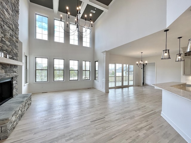 unfurnished living room featuring light hardwood / wood-style floors, a chandelier, a high ceiling, and a stone fireplace