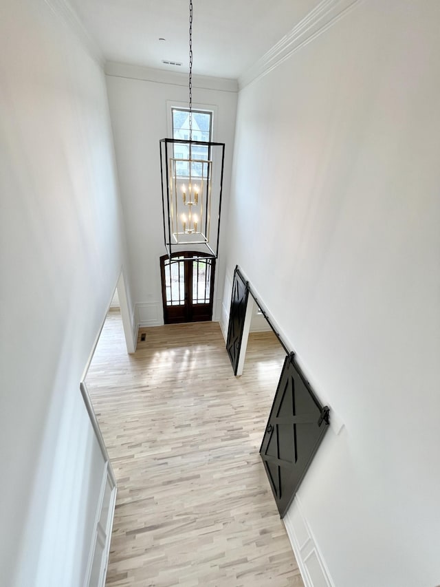 entrance foyer with a high ceiling, french doors, ornamental molding, a notable chandelier, and light hardwood / wood-style flooring