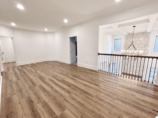 spare room featuring an inviting chandelier, beam ceiling, hardwood / wood-style floors, and coffered ceiling