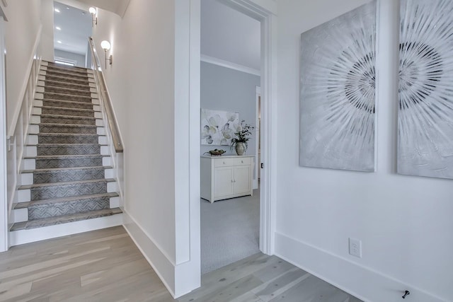 stairs with wood-type flooring and ornamental molding