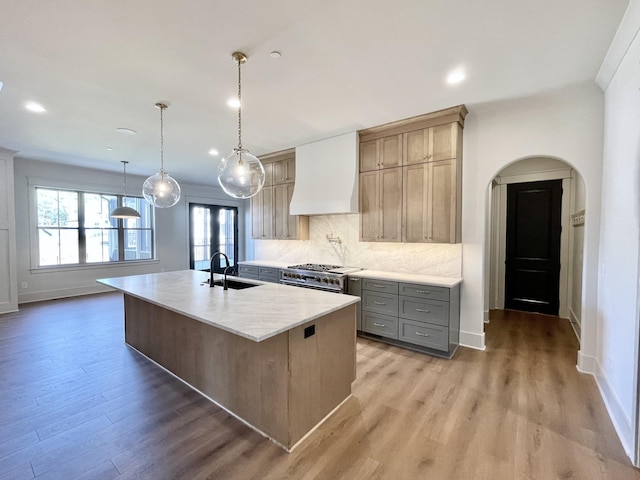 kitchen featuring custom exhaust hood, an island with sink, decorative backsplash, sink, and hanging light fixtures