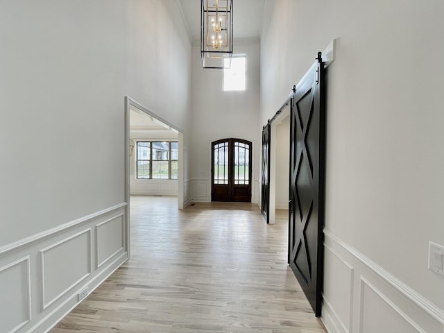 hallway featuring ornamental molding, light wood-type flooring, a chandelier, and a barn door