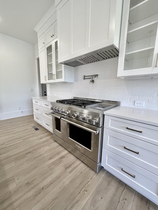 kitchen with white cabinetry, light wood-type flooring, double oven range, and custom range hood