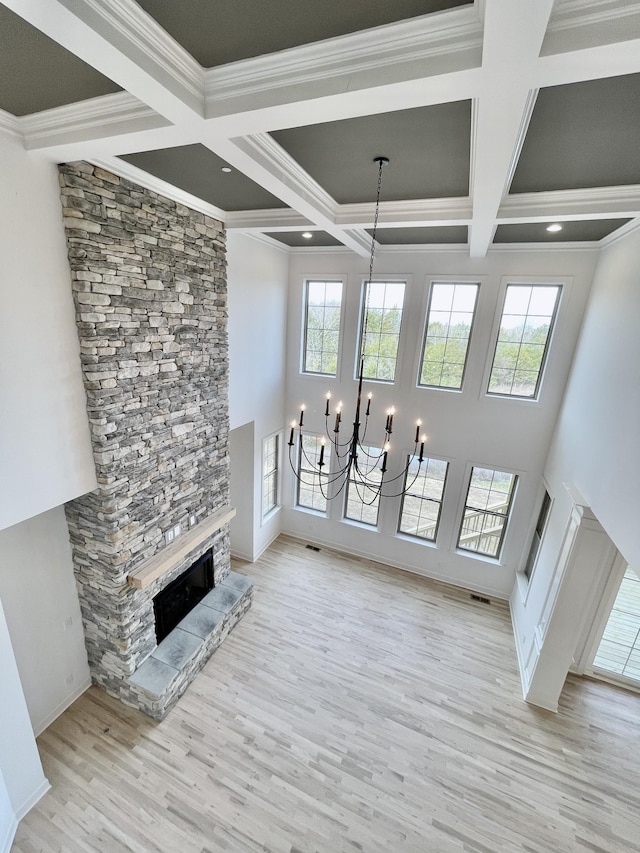 unfurnished living room featuring a stone fireplace, a notable chandelier, light hardwood / wood-style flooring, crown molding, and coffered ceiling