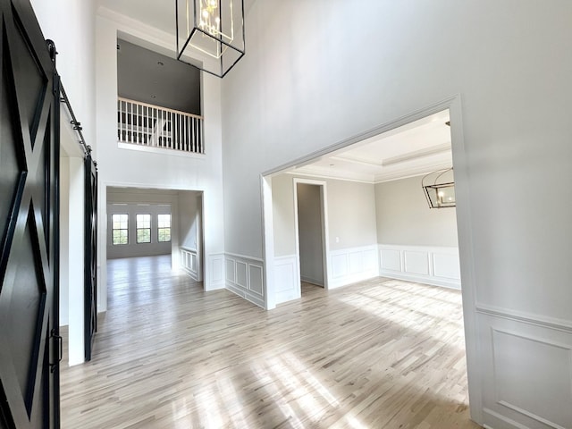 interior space with light hardwood / wood-style flooring, ornamental molding, a barn door, and a notable chandelier