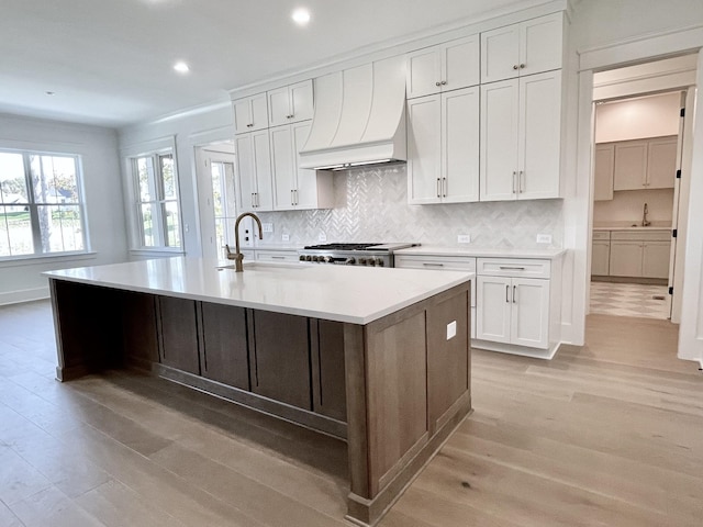 kitchen featuring white cabinets, a kitchen island with sink, light wood-type flooring, and custom range hood