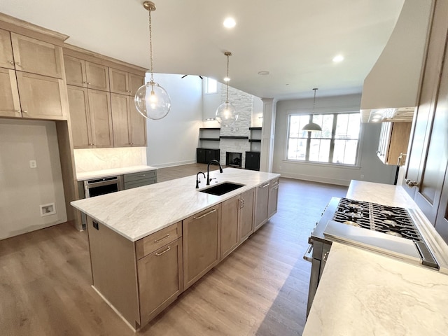 kitchen featuring sink, a center island with sink, light wood-type flooring, and ventilation hood