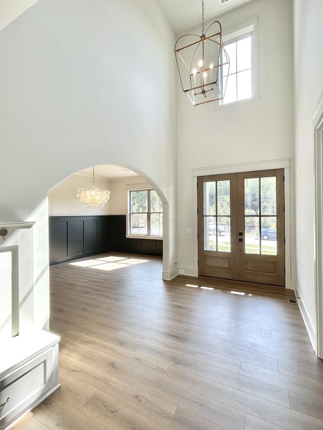 interior space with a towering ceiling, hardwood / wood-style floors, french doors, and an inviting chandelier